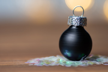 Naklejka na ściany i meble Close-up of a black christmas bauble on a wooden surface with light bokeh background