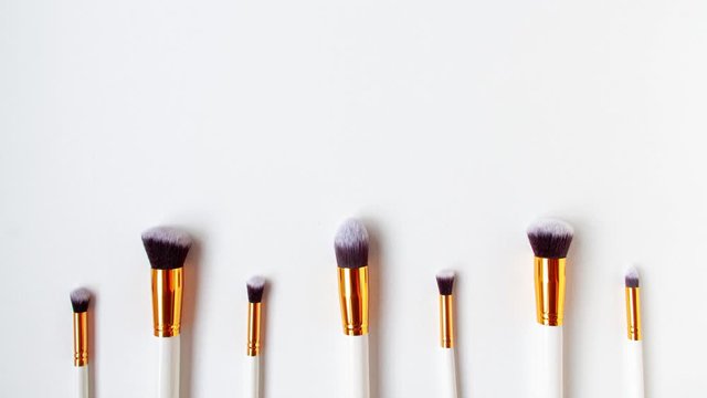 4K stop motion top view of cosmetics brushes set for makeup, which are move up and down the bottom on white background. Cosmetics and beauty concept. Make up concept with space for text