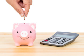 Piggy bank with hand putting insert coin and calculator, on wooden desk, over white background, saving concept