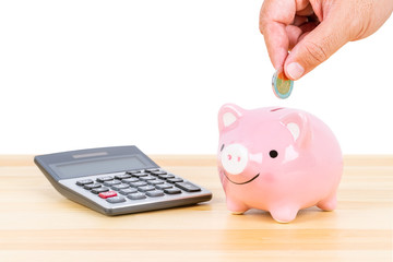 Piggy bank with hand putting insert coin and calculator, on wooden desk, over white background,...