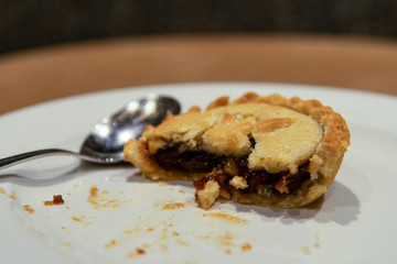 Half eaten Christmas mince pie. Fruit mince pies for festive, winter season.  Mince pie on white plate and silver spoon. Holidays concept. Treat for Santa Claus. Selective focus.