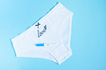 Female white panties with bow and word love and positive pregnancy test on blue . Health care, contraception and planned pregnancy