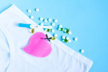 Female white panties with bow, birth control pills or vitamin, paper heart and positive pregnancy test on blue background. Health care, contraception and planned pregnancy
