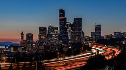 Seattle skyline, at sunset. The cars along the highway are creating light trails, due to a slow...