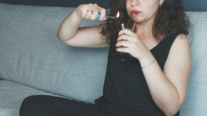 The young person smoking medical marijuana with bong, indoors. The young woman smoke cannabis at...