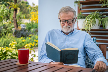 Senior elderly man reading book with mug of coffee in garden