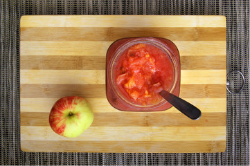 Tasting fresh jam. Bright pink apple jam in a white bowl and pink speckled apple on a striped bamboo kitchen board.