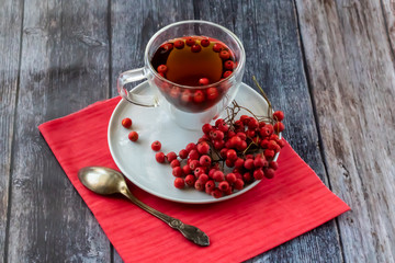 Hot healing tea, mountain ash tea. Reduces the level of harmful cholesterol in the blood, strengthens blood vessels. healing drink on a wooden background with a red napkin