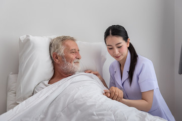 Happy nurse taking care elderly man with blanket in bedroom at nursing home