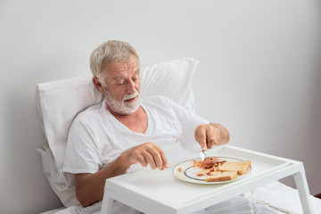 Elderly senior man eating breakfast on bed in bedroom at nursing home