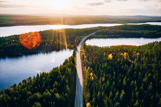Aerial view of bridge across blue lakes with sun light in colorful autumn forest in Finland.