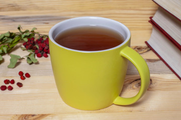 Big ceramic green cup of tea with dry rowan berries and three red cover books on wooden background