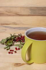 Big ceramic green cup of tea with dry rowan berries on wooden background vertical