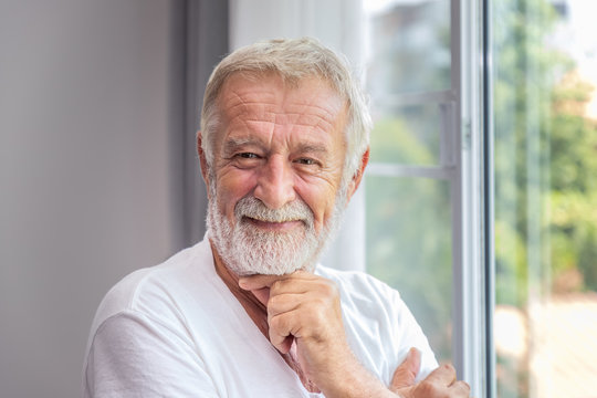 Senior Elderly Man Standing At Window In Bedroom After Waking Up In Morning, Looking Camera