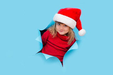 Happy smiling kid in a red sweater and Santa red hat poses through torn paper hole.  Effect of torn paper. Christmas sales.