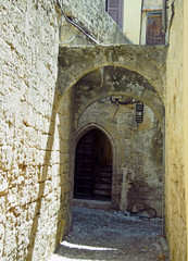 narrow alleyway in rhodes old town with arches between old stone walls and an open doorway with stairs inside