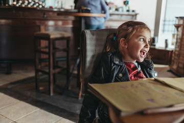 Adorable preschool girl drawing with wooden pencils in a cozy cafe. Cute daughter smiling and drawing colorful shapes for kindergarten homework