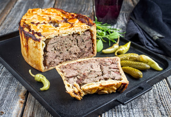 Traditional French pate en croute with goose liver as closeup with gherkin and pepperoni on a modern design cast iron tray