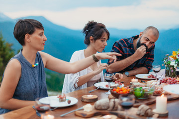 Friends and family gathered for picnic dinner for Thanksgiving. Festive young people celebrating life with red wine, grapes, cheese platter, and a selection of cold meats