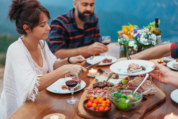 Friends and family gathered for picnic dinner for Thanksgiving. Festive young people celebrating life with red wine, grapes, cheese platter, and a selection of cold meats
