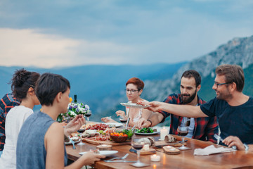 Friends and family gathered for picnic dinner for Thanksgiving. Festive young people celebrating life with red wine, grapes, cheese platter, and a selection of cold meats