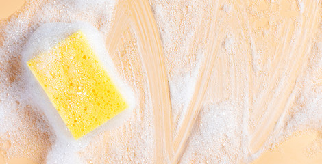 Yellow sponge for cleaning in foam on a soft beige background, top view, free space for text. House cleaning with sponge. Cleaning concept, copy space.