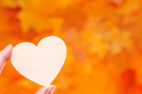 Wooden heart symbol in hand on orange background. Love concept