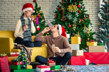 Obraz na płótnie Canvas Happy couple beautiful woman and man in santa hat enjoying and celebrating family Christmas party together at home with drinking white wine or champagne with decoration Christmas tree background.