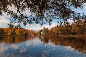 Colorful trees and a beautiful rotunda on the banks of a pond in a park on a sunny autumn evening