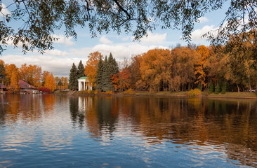 Colorful trees and a beautiful rotunda on the banks of a pond in a park on a sunny autumn evening