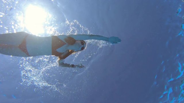 bottom view underwater of woman swimming crawl style and behind six years child in clear water of pool or sea