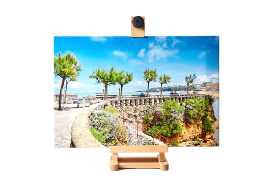 Wooden easel with canvas photo print isolated on white background. Front view of colorful photography printed on glossy synthetic canvas