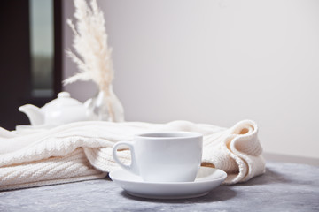 Cup of hot aroma coffee and knittead white plaid and white teapot on the gray table