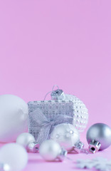 Silver Christmas baubles and gift box on a light pink background