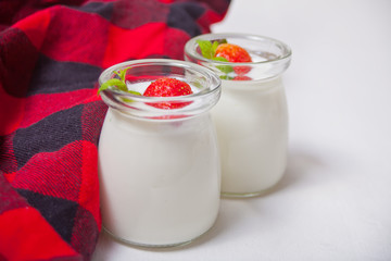 Two portions natural homemade yogurt in a glass jar with fresh strawberry with red checkered napkin on the white background