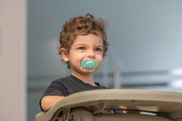 Close-up to the adorable child face with brown hair and a pacifier in the mouth, with the background out of focus. Concept of innocence and child tranquillity.