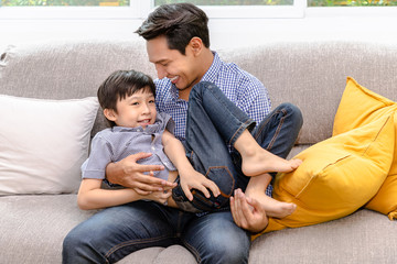 Happy Asian father playing and carry his son on sofa in living room at home, family relationship...