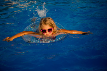little blonde girl in sunglasses swims in pool with swimming circle
