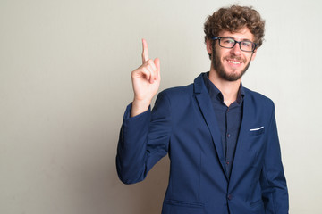 Fototapeta premium Happy young bearded businessman with eyeglasses in suit pointing up