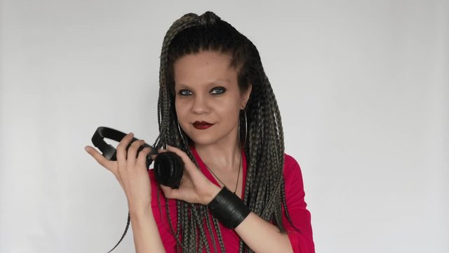 A gothic girl in a crimson top with long grey afro braids and a dark make up is listening to music in giant headphones. This music lover is enjoying the sound. A creative concept for a music gear stor