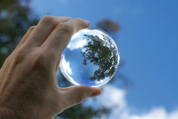 hand of man holding a lensball in front of blue sky green trees forest mirror reflect circle
