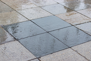 The urban street surface of the road is wet, the street is paved with square gray black granite...