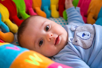 Portrait of a baby lying and surrounded by a colorful stuffed worm.