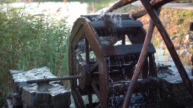 The pressure of water rotates an old water mill. Spray flying in different directions