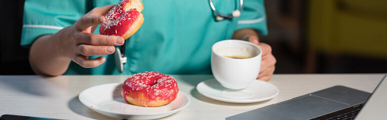 panoramic shot of nurse in uniform holding donut and cup during night shift