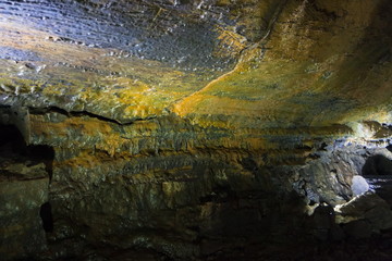 The wall of the lava cave is covered with a yellow fungal coating. The view opening in front of cavers