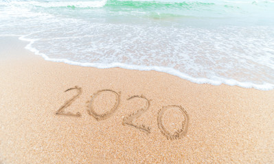 Happy New Year 2020 written on seashore sand at sunrise concept.beautiful sandy beach and soft blue ocean wave