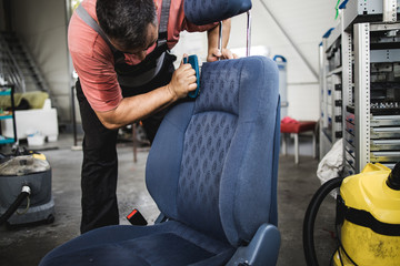 An auto service worker prepares and cleans the car seat