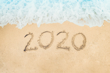 Happy New Year 2020 written on seashore sand at sunrise concept.beautiful sandy beach and soft blue ocean wave
