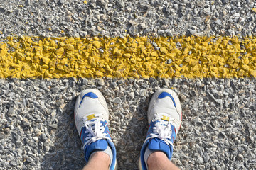 Fototapeta premium man stands on the asphalt road before yellow border line in white sneakers close-up